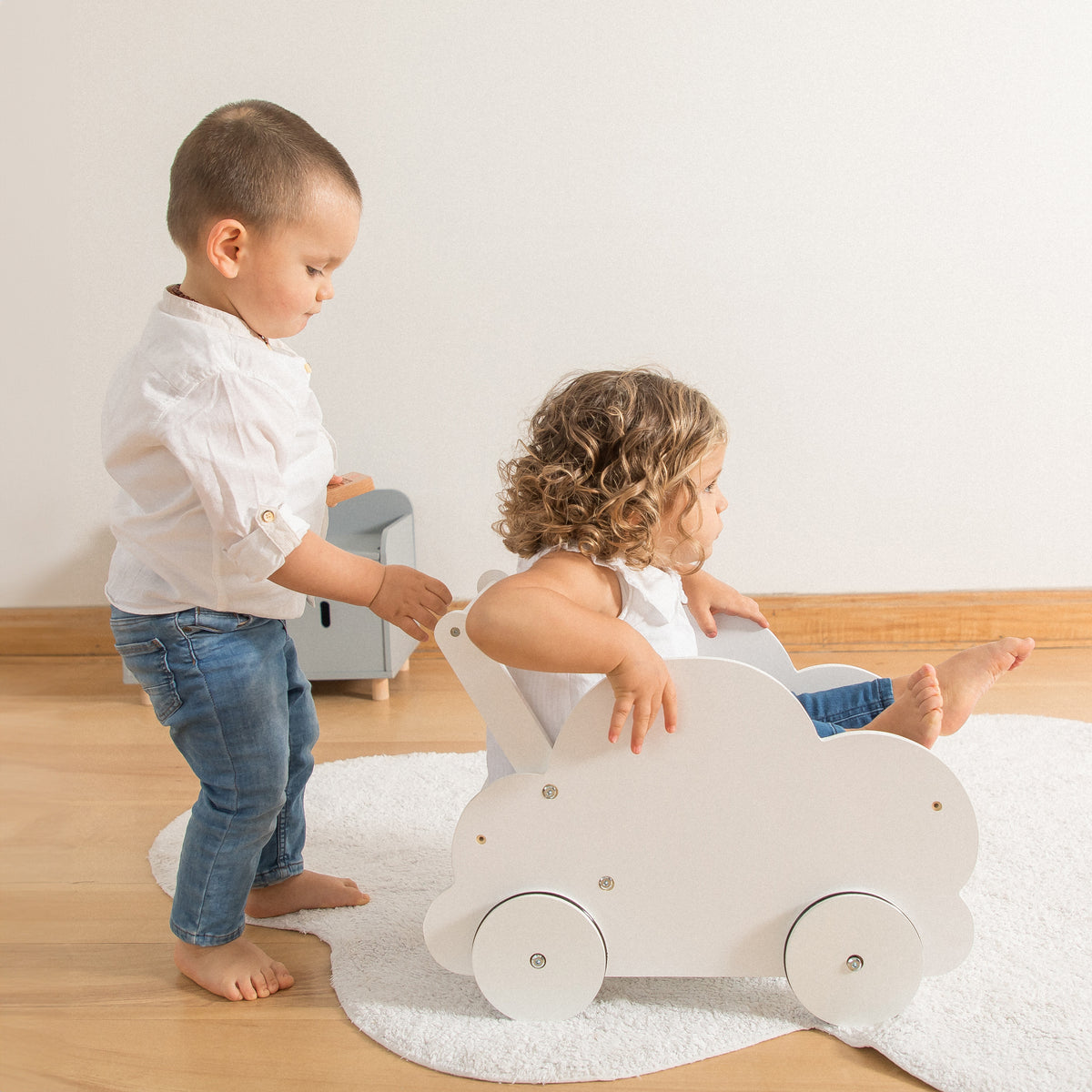 Juguete de coche infantil de madera con diseño de nube blanca siendo utilizado por dos niños pequeños dentro de casa