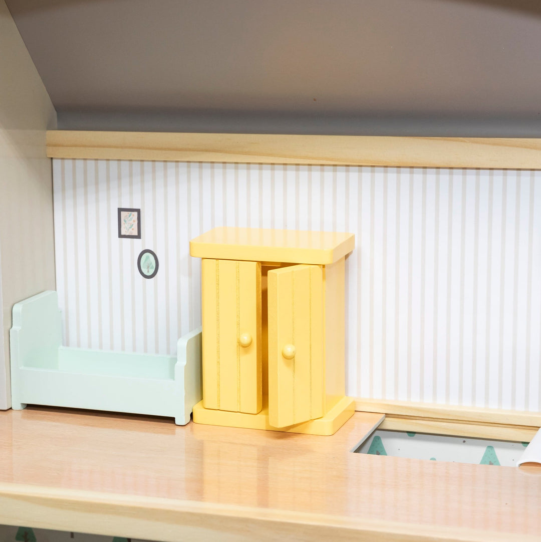 Vista interior del dormitorio de la casa de muñecas, con cama y armario de madera en miniatura.