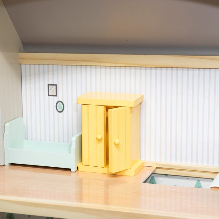 Vista interior del dormitorio de la casa de muñecas, con cama y armario de madera en miniatura.