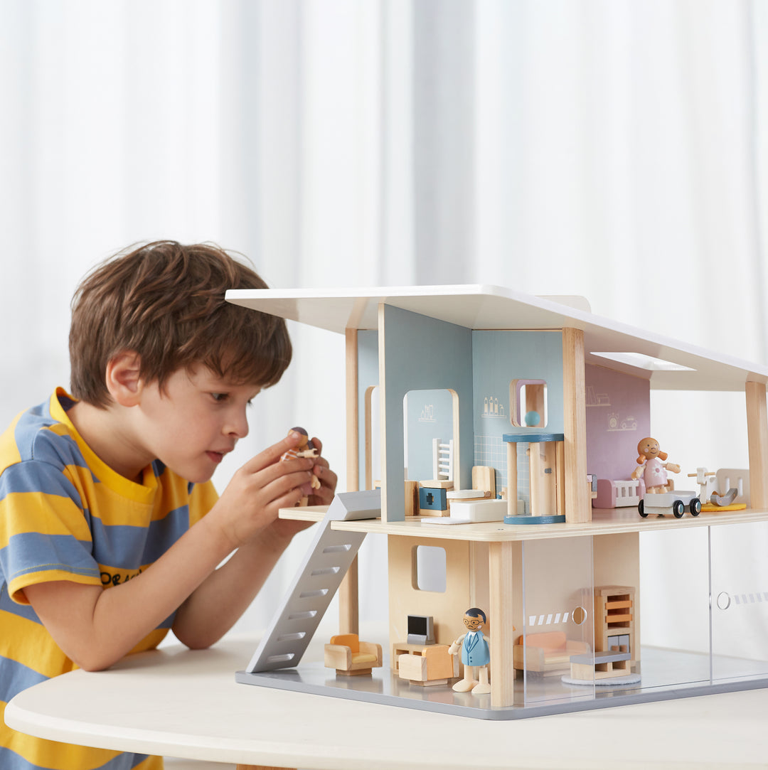 Niño jugando con una casa de muñecas de dos pisos con accesorios y figuras.
