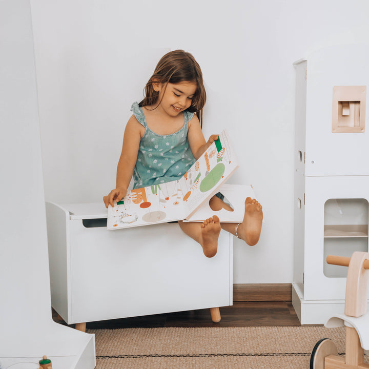 Niña sentada sobre baúl de juguetes blanco de madera, organizador infantil para piezas de niños con diseño moderno