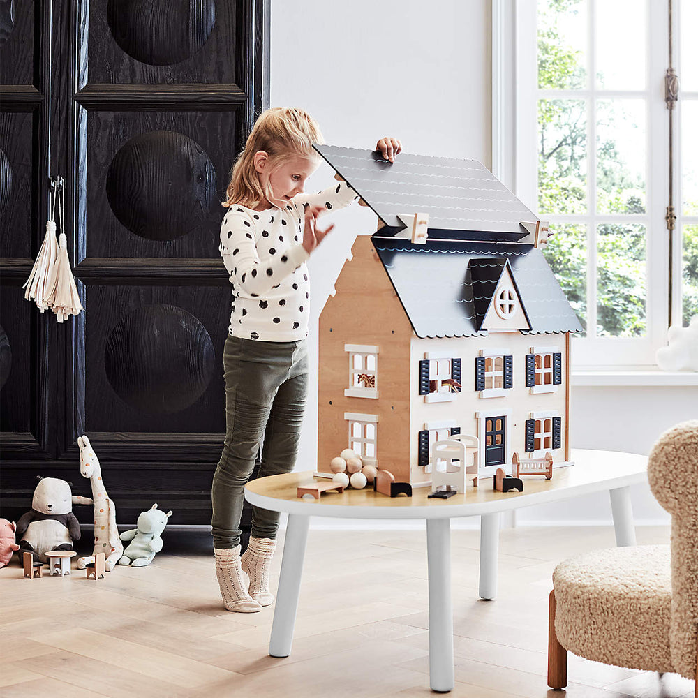 Niña jugando con una casa de muñecas grande de madera y accesorios, promoviendo el juego de rol.