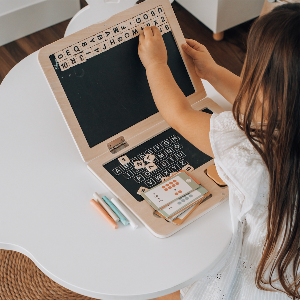 Niño jugando con computador didáctico de madera con pizarra imantada