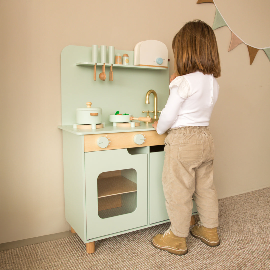 Niño jugando con cocina de juguete verde de madera estilo Montessori