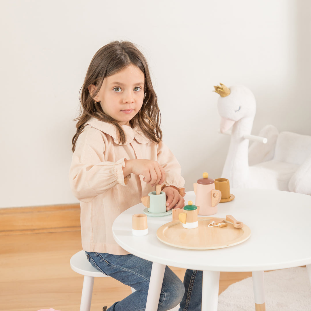 Niña jugando con set de té de madera en tonos pastel, juego simbólico para niños