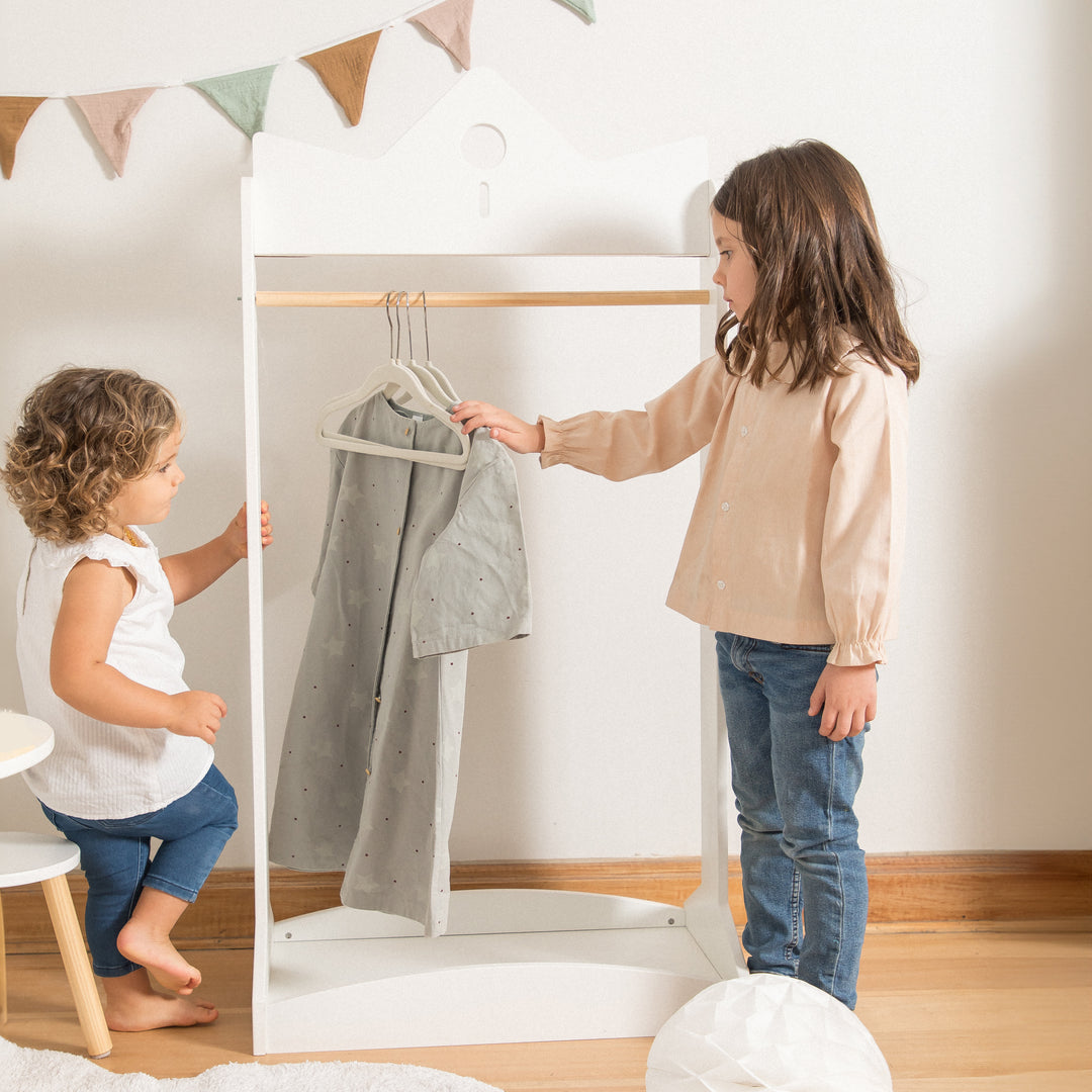 Niñas organizando ropa en perchero infantil de madera blanco, mobiliario estilo Montessori ideal para fomentar la autonomía
