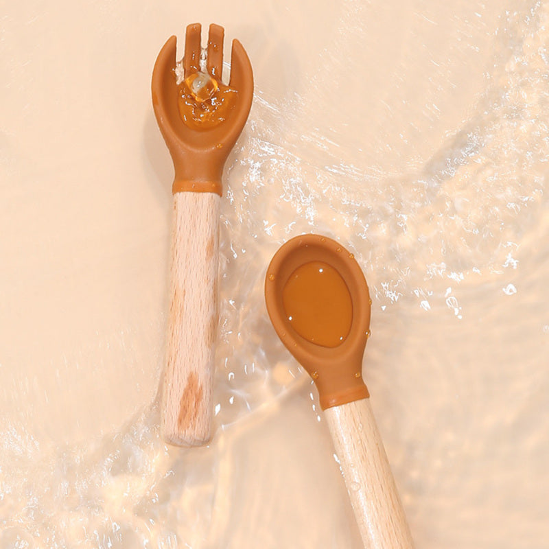 Cubiertos de silicona y madera para bebé color ocre sobre agua, ideales para alimentación complementaria