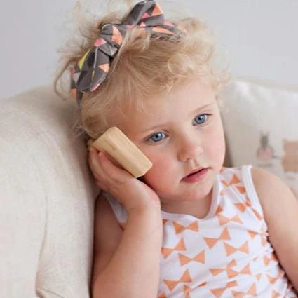 Niña pequeña usando teléfono de madera de juguete para juego de imitación